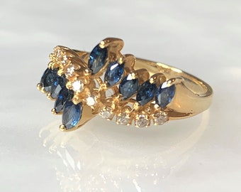 May include: A gold ring with a cluster of marquise-shaped blue sapphires and small round diamonds. The ring has a delicate, intricate design.