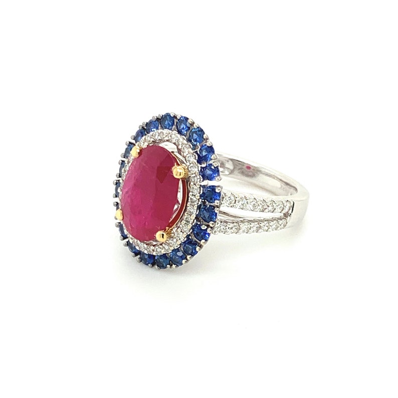 Op de afbeelding: Een zilveren ring met een grote ovale robijn omringd door een halo van kleinere diamanten en saffieren.