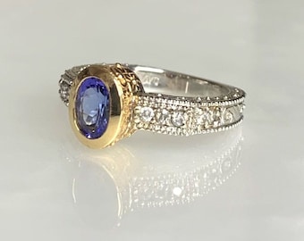 Peut inclure: Une bague en or et argent avec une pierre ovale bleue entourée de petits diamants. La bague a un design détaillé sur la bande.