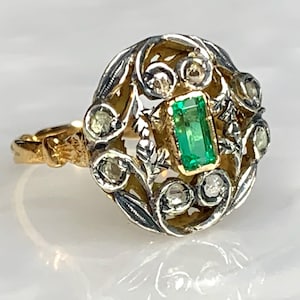 May include: A vintage ring with a green emerald gemstone surrounded by smaller diamonds set in a gold and silver filigree design.