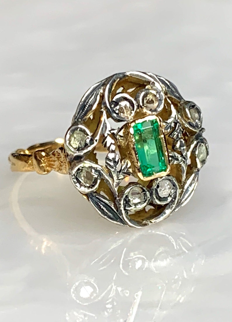 May include: A vintage ring with a green emerald gemstone surrounded by smaller diamonds set in a gold and silver filigree design.
