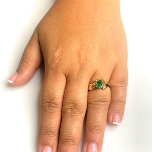 Peut inclure: Une bague en or avec une pierre pr&eacute;cieuse verte sertie dans une bande torsad&eacute;e. La bague est port&eacute;e &agrave; l'annulaire d'une main aux ongles manucur&eacute;s.