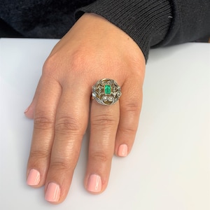 May include: A gold ring with a green emerald gemstone surrounded by smaller diamonds in a floral design.
