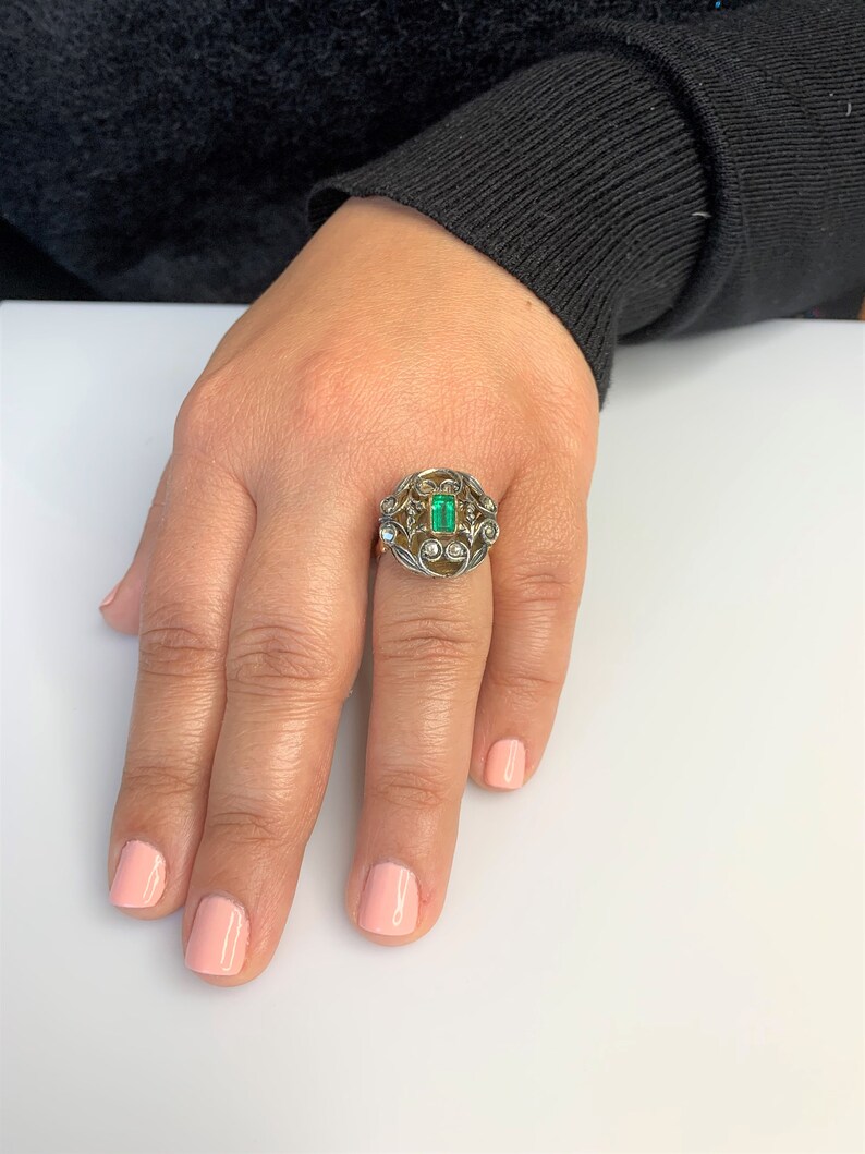May include: A gold ring with a green emerald gemstone surrounded by smaller diamonds in a floral design.