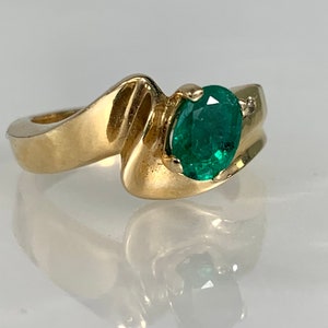 Peut inclure: Une bague en or avec une &eacute;meraude verte et un petit accent diamant. La bague a un design unique et ondul&eacute;.