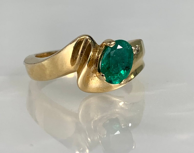 Peut inclure: Une bague en or avec une &eacute;meraude verte et un petit accent diamant. La bague a un design unique et ondul&eacute;.