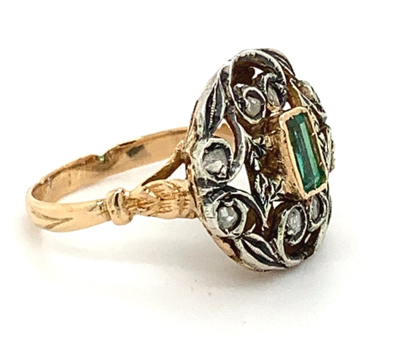 May include: A gold and silver ring with a green emerald gemstone and small diamonds set in a floral design.