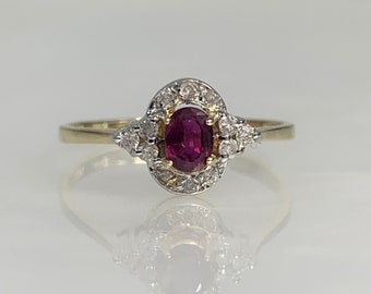 May include: A gold ring with a red oval ruby surrounded by a halo of small diamonds.