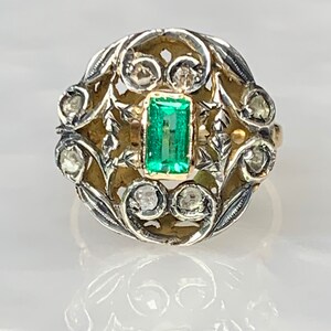 May include: A vintage ring with a green emerald gemstone set in a gold filigree design. The ring is accented with small diamonds.