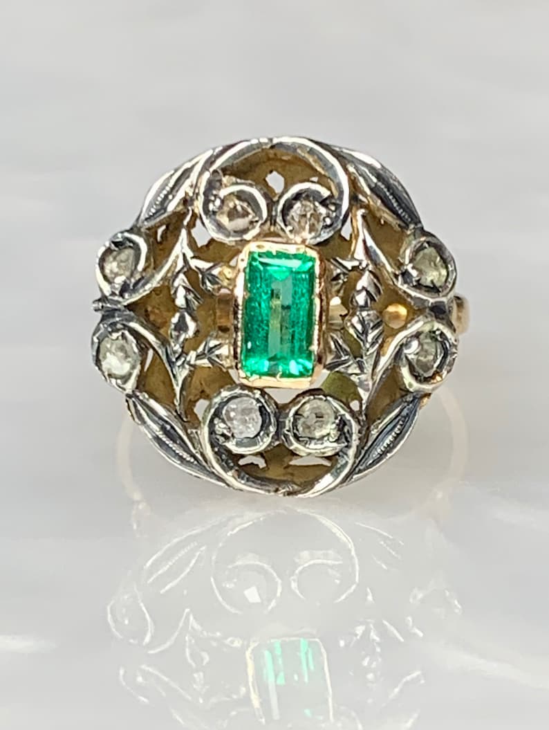 May include: A vintage ring with a green emerald gemstone set in a gold filigree design. The ring is accented with small diamonds.