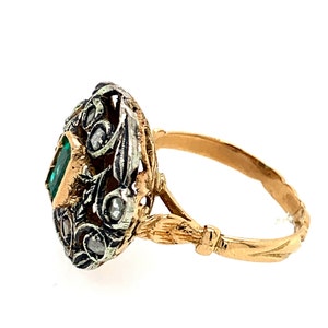 May include: A gold ring with a green emerald gemstone set in a silver filigree design. The ring band is gold with a twisted design.