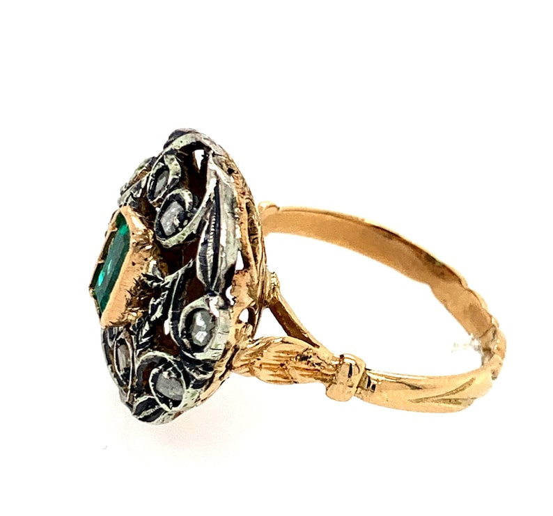 May include: A gold ring with a green emerald gemstone set in a silver filigree design. The ring band is gold with a twisted design.