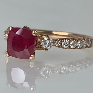 Puede incluir: Un anillo de oro con una gran piedra de rub&iacute; roja cuadrada rodeada de diamantes m&aacute;s peque&ntilde;os. La banda est&aacute; engastada con una fila de diamantes m&aacute;s peque&ntilde;os.