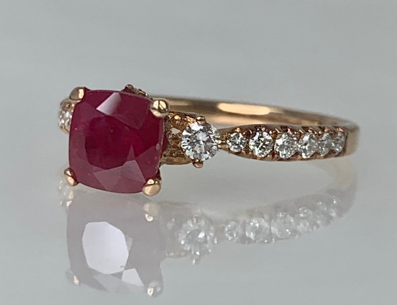 Puede incluir: Un anillo de oro con una gran piedra de rub&iacute; roja cuadrada rodeada de diamantes m&aacute;s peque&ntilde;os. La banda est&aacute; engastada con una fila de diamantes m&aacute;s peque&ntilde;os.