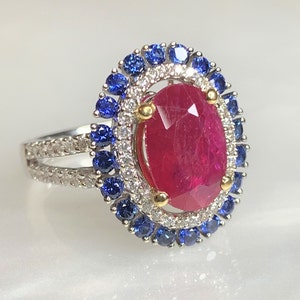 Op de afbeelding: Een ring met een grote ovale robijn omringd door een halo van kleinere diamanten en blauwe saffieren.
