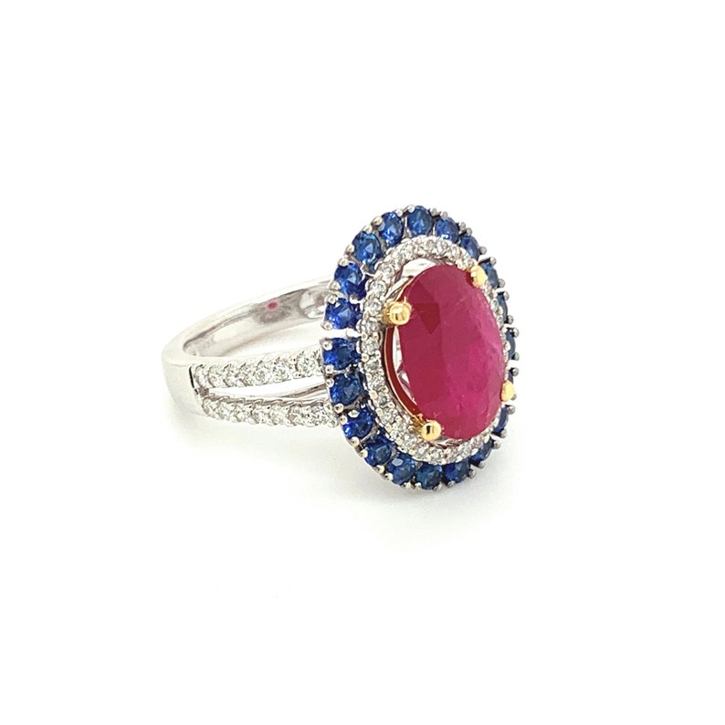 Op de afbeelding: Een ring met een grote ovale robijn, omringd door een halo van kleinere diamanten en saffieren.