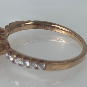 Puede incluir: Un anillo de oro con una piedra preciosa grande rodeada de piedras m&aacute;s peque&ntilde;as. El anillo est&aacute; grabado con "750 DO.34".