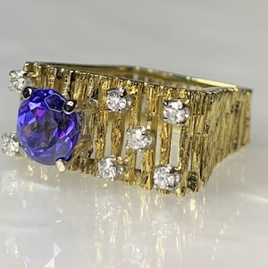 May include: A gold ring with a large purple gemstone surrounded by smaller diamonds. The band is textured and has a unique design.
