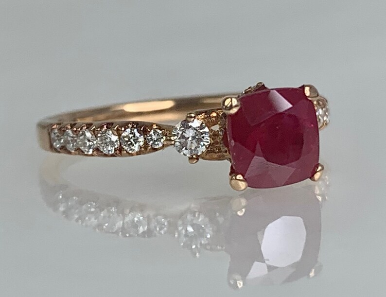 Puede incluir: Un anillo de oro rosa con una gran piedra preciosa de rub&iacute; rojo y diamantes m&aacute;s peque&ntilde;os engastados en la banda.