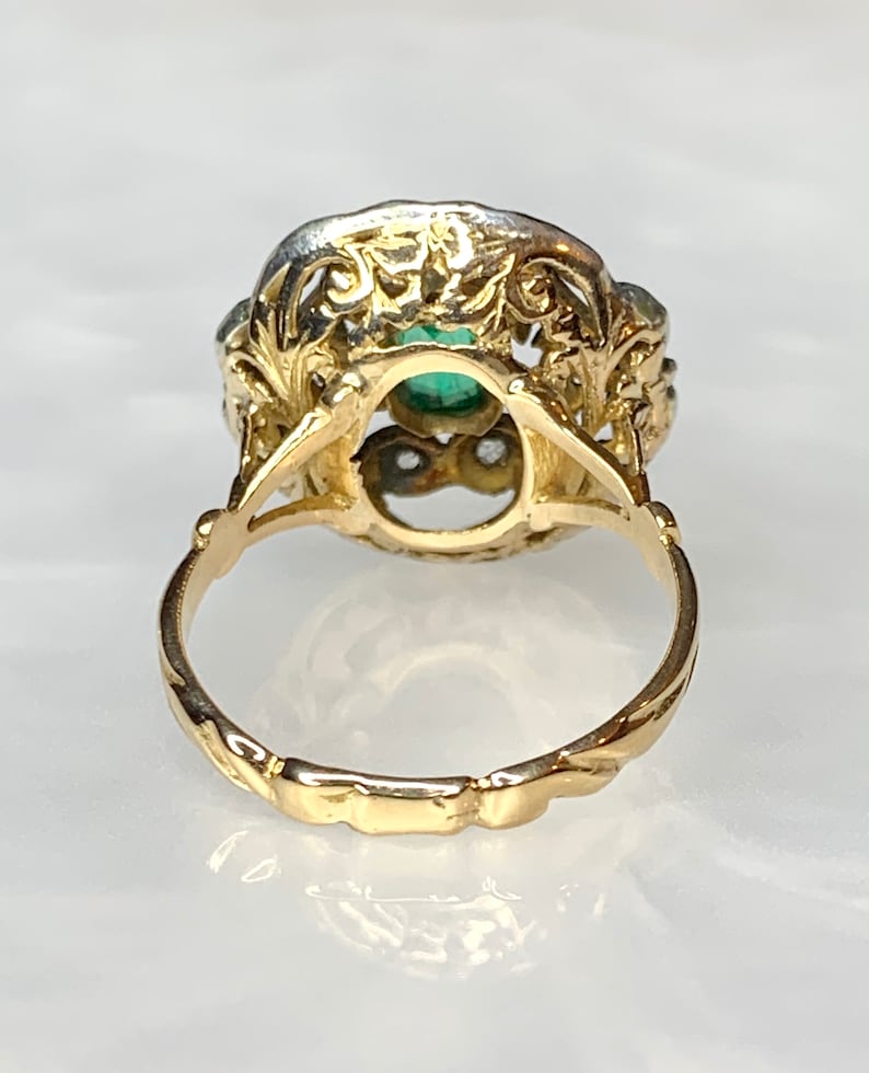 May include: A gold ring with a green gemstone set in a filigree design. The ring has a twisted band.