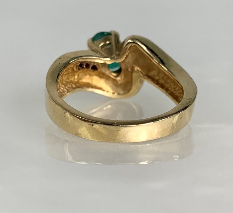 Peut inclure: Une bague en or avec une pierre pr&eacute;cieuse verte sertie dans une bande torsad&eacute;e. La bague est sertie de pierres pr&eacute;cieuses plus petites sur la bande.