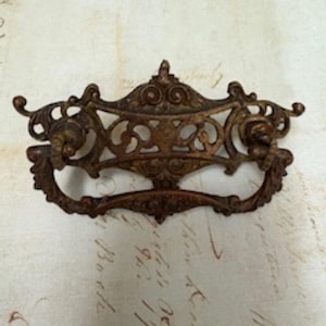 May include: Ornate, antique bronze drawer pull with intricate scrollwork and decorative elements. The handle features a curved design with detailed carvings and a warm, aged patina, perfect for vintage furniture restoration.