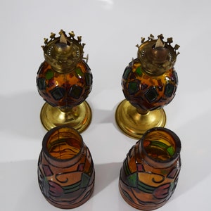 May include: Four stained glass oil lamps with gold bases. The lamps are decorated with geometric patterns in shades of brown, green, and red.