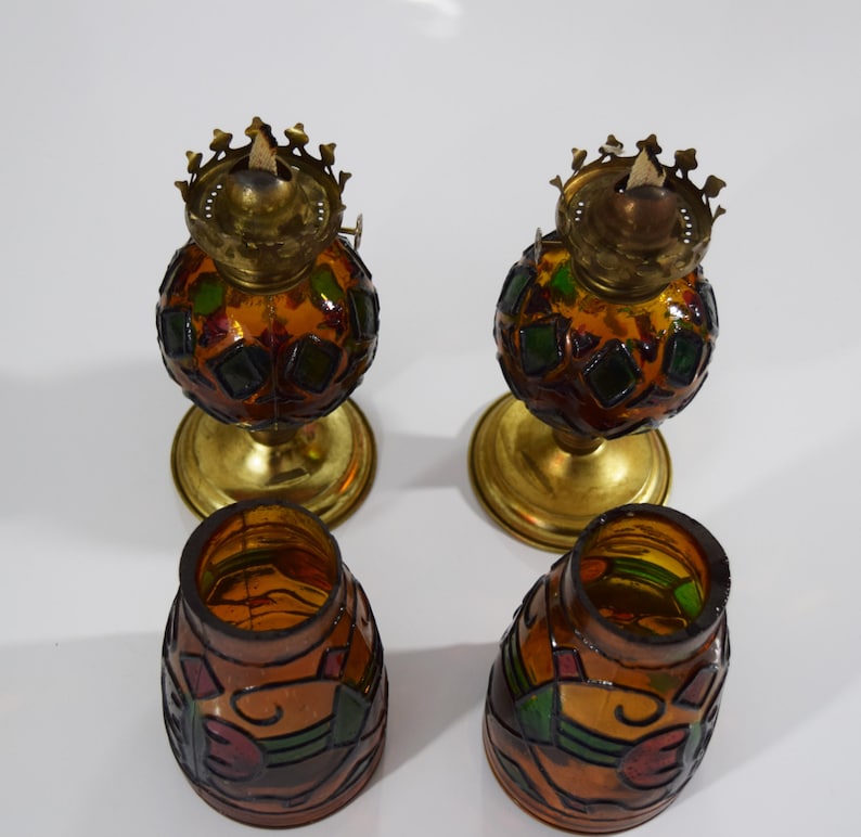 May include: Four stained glass oil lamps with gold bases. The lamps are decorated with geometric patterns in shades of brown, green, and red.