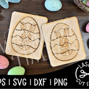 May include: Two wooden Easter egg puzzle pieces with bunny designs. The top piece has the name "Emedy" and the bottom piece has the name "Quincy".