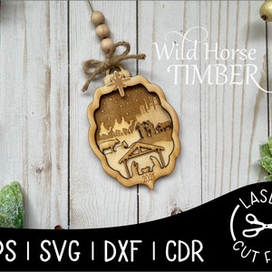May include: A wooden Christmas ornament featuring a laser-cut nativity scene with the year 2021 inscribed. The ornament is decorated with a brown twine bow and a string of wooden beads. The text "Wild Horse Timber" is visible in the upper right corner of the image.