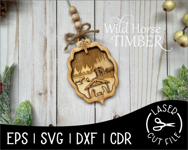 May include: A wooden Christmas ornament featuring a laser-cut nativity scene with the year 2021 inscribed. The ornament is decorated with a brown twine bow and a string of wooden beads. The text "Wild Horse Timber" is visible in the upper right corner of the image.