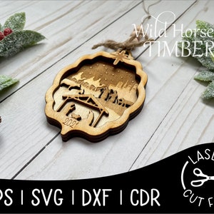 May include: A wooden Christmas ornament featuring a nativity scene with the year 2021 engraved on the bottom. The ornament is laser cut and has a rustic brown finish. The text "Wild Horse Timber" is visible in the background.