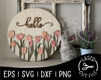 Könnte beinhalten: Ein rundes Holzschild mit dem Wort "hello" in Kursivschrift und einem Rand aus rosa Tulpen. Das Schild hängt an einer weiß getünchten Holzwand.