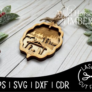May include: A wooden Christmas ornament featuring a nativity scene with the year 2021 engraved on the bottom. The ornament is laser cut and has a rustic brown finish. The text "Wild Horse Timber" is visible in the background.