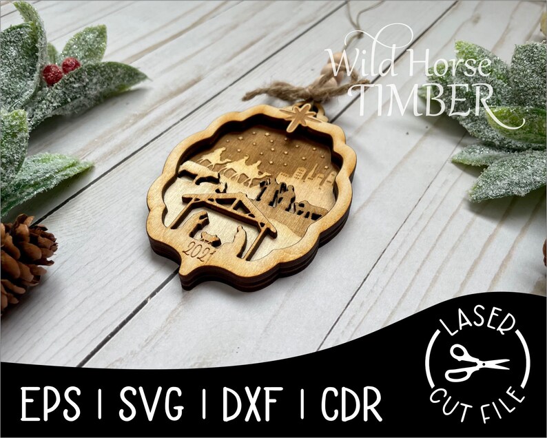 May include: A wooden Christmas ornament featuring a nativity scene with the year 2021 engraved on the bottom. The ornament is laser cut and has a rustic brown finish. The text "Wild Horse Timber" is visible in the background.