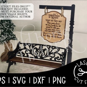 May include: A wooden sign with the text "Christmas in Heaven" and a poem about loved ones who have passed away. The sign is hanging on a black metal stand with a black metal bench in front of it. There are two small snow-covered trees on either side of the bench.