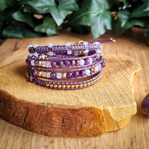 Peut inclure: Un bracelet multi-rangs avec des perles violettes et blanches, des accents dorés et une base en cuir.