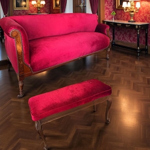 May include: A red velvet sofa and matching bench with wooden frames. The sofa has curved arms with decorative wood trim. The bench is rectangular with curved legs. The furniture sits on a dark wood floor.