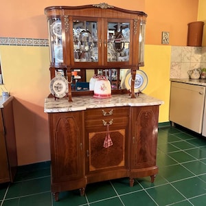 May include: A wooden hutch with a marble-patterned countertop, featuring a glass-fronted upper cabinet with two doors, a central mirror, two drawers, and two lower cabinets. The furniture is adorned with gold-toned metal hardware and decorative accents.