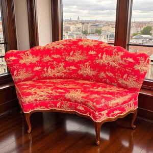 May include: A red settee with a curved back and armless design. The fabric features a toile pattern in beige and red. The settee has wooden legs and is placed near a window with a city view.