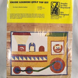May include: A quilt top kit featuring a train engine with a lion, bell, and umbrella applique. The kit includes cotton-polyester blend fabrics, easy-to-follow instructions, and a zipper pocket. The kit is 32 inches by 42 inches.  Kit #250K. Copyright 1979. Needle-In-The-Haystack, Inc. 306 S. Lookout Mtn. Rd. Golden, CO 80401.