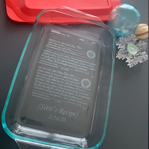 Puede incluir: Un plato para hornear de vidrio transparente con una receta escrita a mano para pollo y arroz amarillo grabada en el fondo. La receta incluye instrucciones para preparar el plato y notas sobre los ingredientes. El plato está etiquetado como "Receta de Sitti" y fechado el 2/14/20.