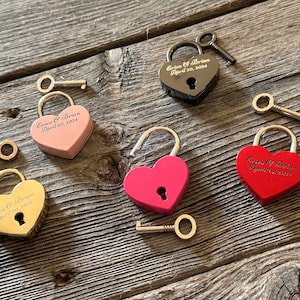 May include: Four heart-shaped padlocks with keys, each engraved with a name and date. The padlocks are in black, pink, gold, and red.