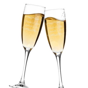 May include: Two champagne flutes clinking together, filled with a golden liquid. Each glass has a slender stem and a wide bowl. The text "Natalie & John, September 2022" is etched on the front of each glass.