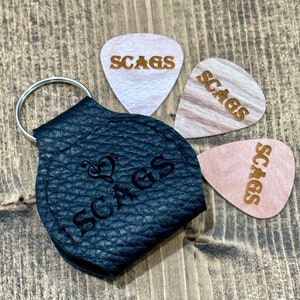 Puede incluir: Un porta-púas de cuero negro con un llavero y la palabra "SCAGS" grabada en relieve. También se incluyen tres púas de madera con la palabra "SCAGS" grabada.