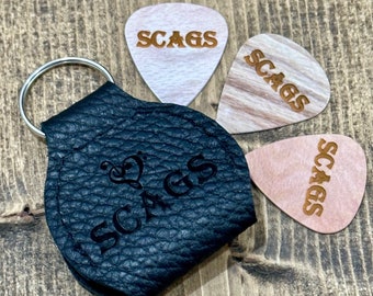Peut inclure: Un porte-médiator en cuir noir avec un porte-clés et le mot "SCAGS" en relief. Trois médiators en bois avec le mot "SCAGS" gravé sont également inclus.