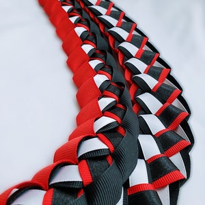 May include: A red, black and white braided ribbon lei. The lei is made of three different colours of ribbon that are woven together to create a decorative pattern.