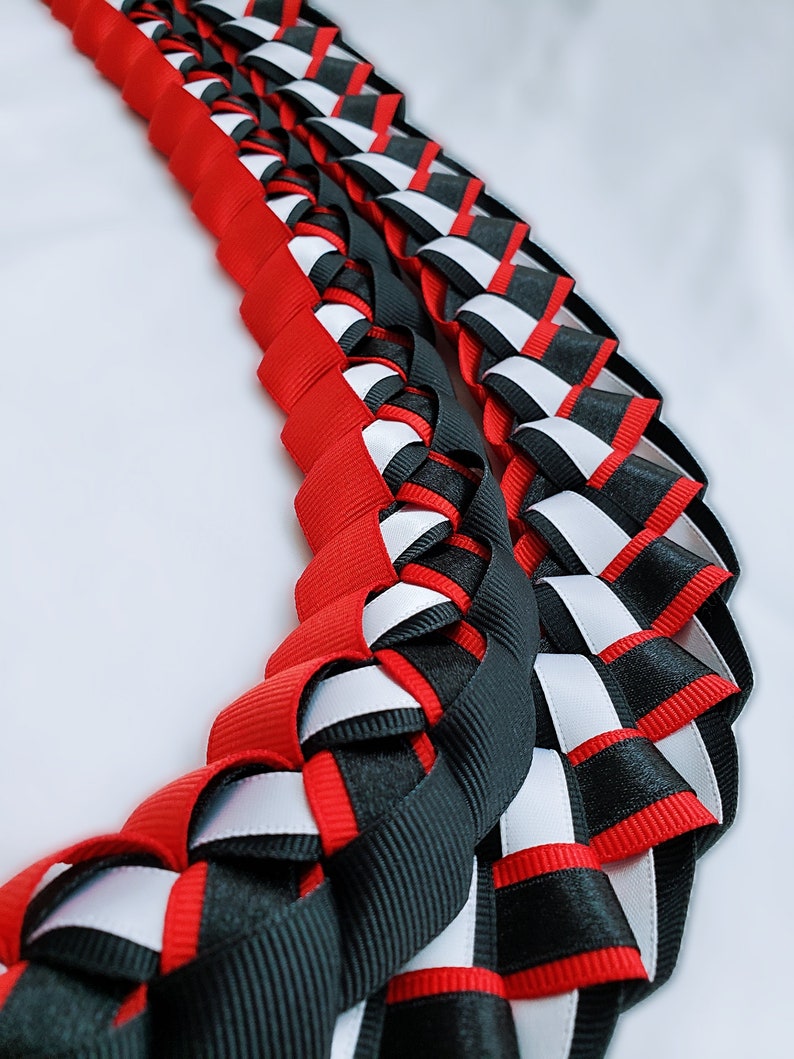 May include: A red, black and white braided ribbon lei. The lei is made of three different colours of ribbon that are woven together to create a decorative pattern.