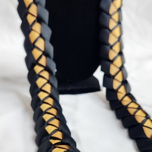 May include: A black and gold lei made of braided ribbon. The lei is a traditional Hawaiian garland worn around the neck.