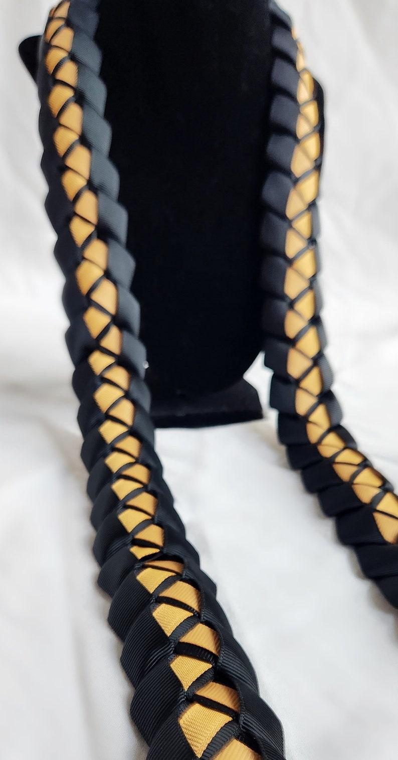 May include: A black and gold lei made of braided ribbon. The lei is a traditional Hawaiian garland worn around the neck.